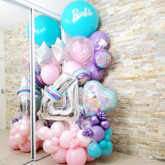 A balloon bouquet featuring a large '4' shaped balloon in silver with purple and pink accents, along with various other balloons in shades of pink and purple, personalized with the name 'Barbie' written on a teal balloon.