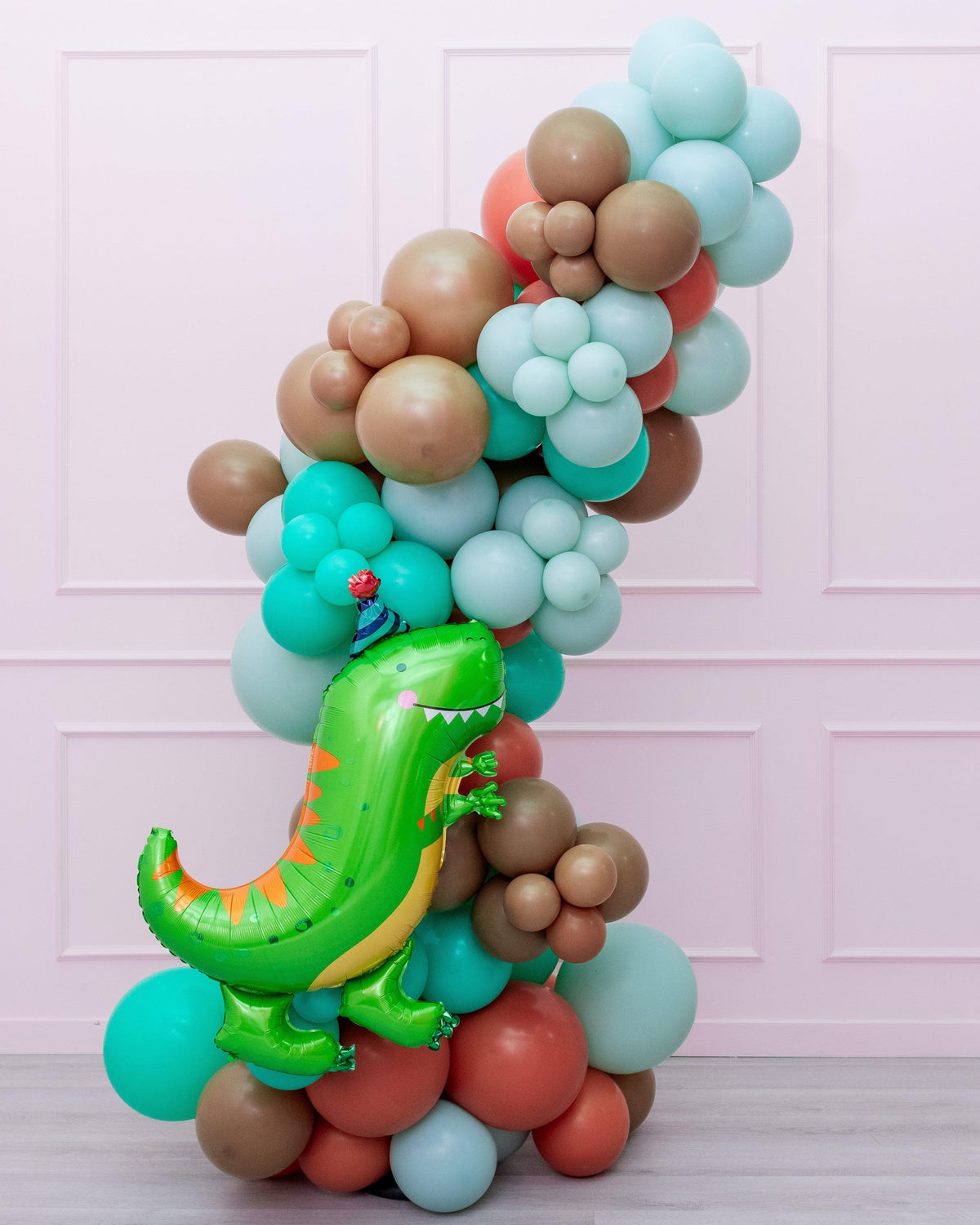 A colorful balloon garland featuring a dinosaur-themed balloon prominently placed amidst a variety of other shapes and colors.