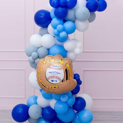 A balloon garland featuring a variety of blue and white balloons shaped like baseballs and a baseball glove, with a prominent baseball-themed balloon at the center.