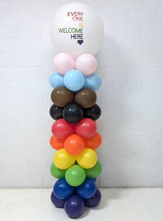 A multicolored balloon column featuring a variety of balloons in different colors stacked vertically, with a prominent pink balloon at the top that reads 'Everyone is Welcome Here'.