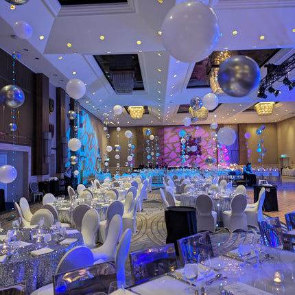 A decorative balloon centerpiece featuring multiple large balloons in varying sizes, held together by a glowing light ribbon, set against a room with a festive atmosphere. Made by Ana Karina Balloons in Toronto