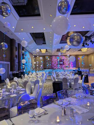 A decorative balloon centerpiece featuring multiple large balloons in varying sizes, held together by a glowing light ribbon, set against a room with a festive atmosphere. Made by Ana Karina Balloons in Toronto