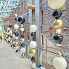 Decorative arrangement of black, white, and gold balloons hanging from a ceiling.