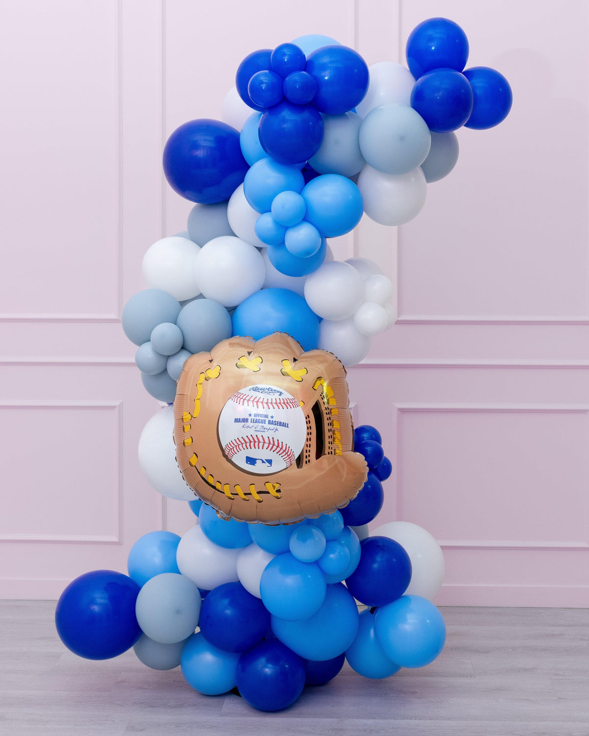 A balloon garland featuring a variety of blue and white balloons shaped like baseballs and a baseball glove, with a prominent baseball-themed balloon at the center.