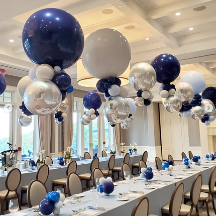 Decorated event room with blue, silver, and white balloons above tables set for a meal.