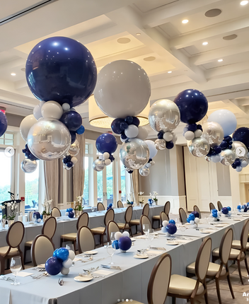 Decorated event room with blue, silver, and white balloons above tables set for a meal.