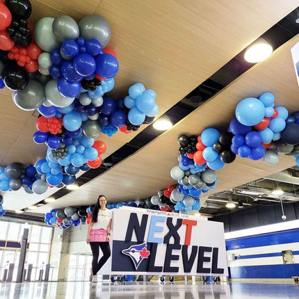 A custom balloon garland featuring a variety of balloons in different sizes and colors, arranged in an organic shape along a wooden pathway with a person standing in front of the garland.