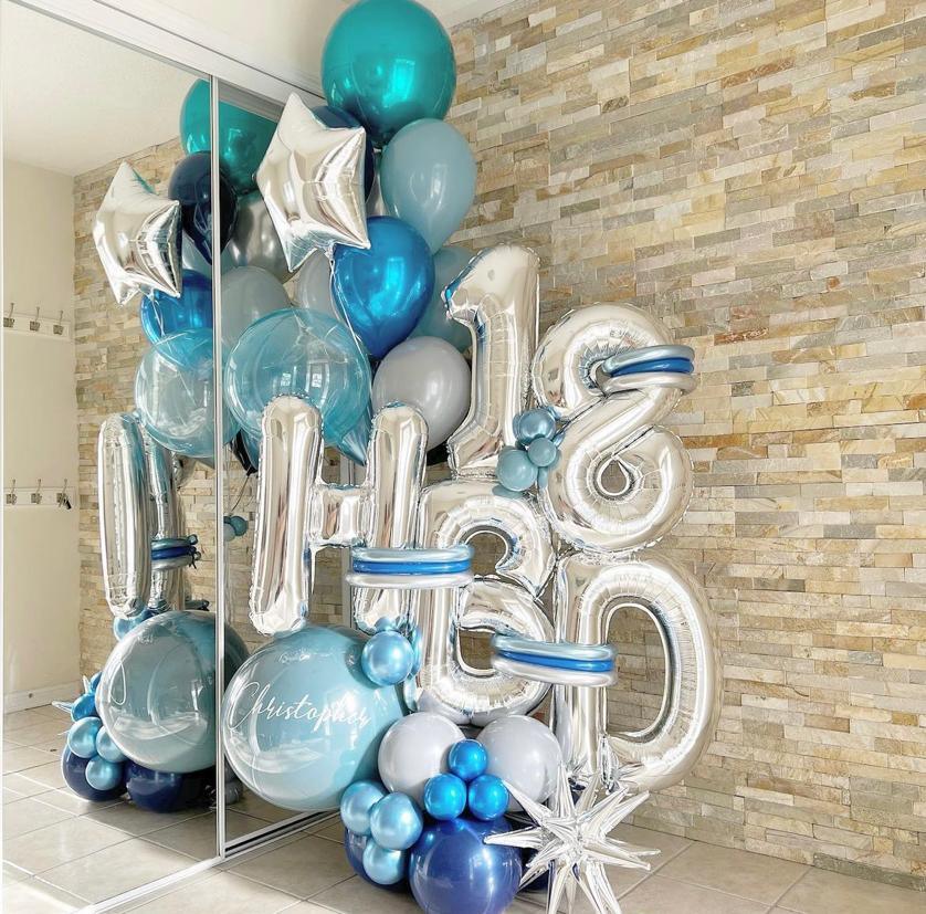 A bouquet of blue foil balloons with the numbers '18' and 'HBD' (short for 'Happy Birthday') arranged in a reflective room with a brick wall and a large mirror.