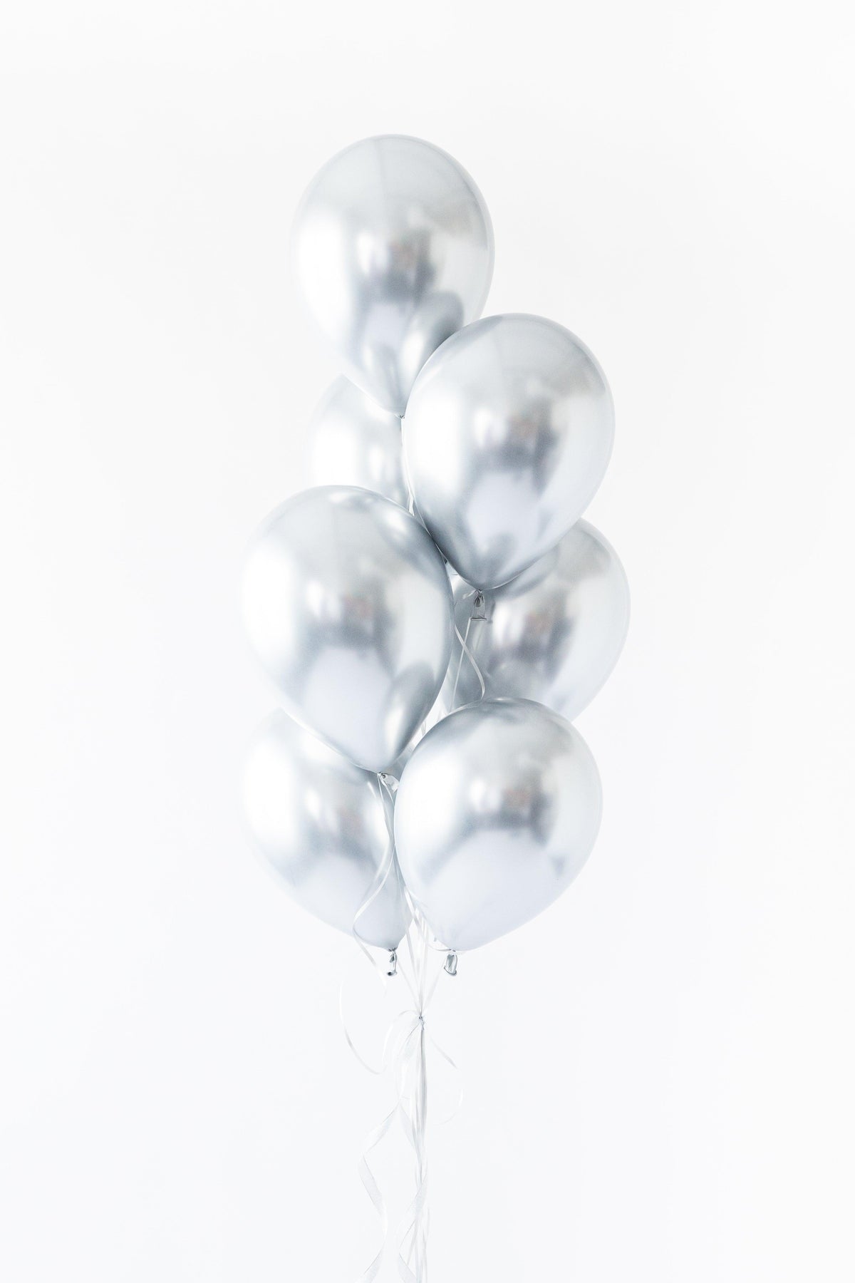 A bunch of silver-colored balloons tied together against a white background.
