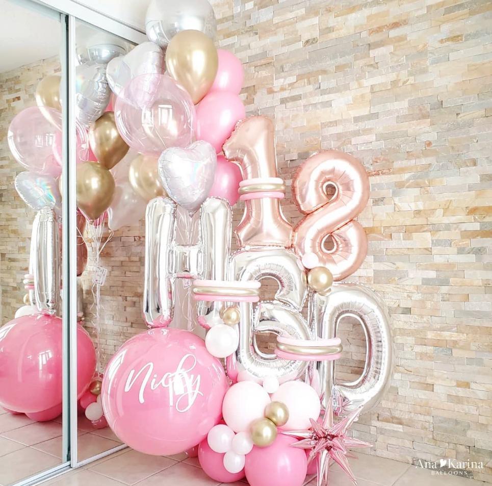 A bouquet of baby pink balloons with gold accents, including foil balloons with the number 18 and other shapes, displayed indoors.