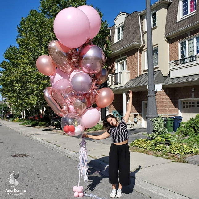 A bunch of pink balloons tied to a balloon pole, with a woman standing on the side of the road holding a balloon.